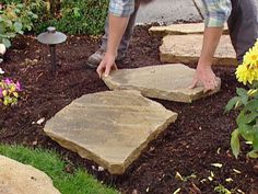 a man is working in the garden with some rocks and flowers on the side walk