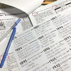 a blue pen sitting on top of an open book next to some papers with numbers