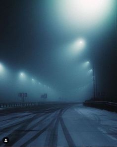 an empty road with street lights in the fog on a cold night, and no cars