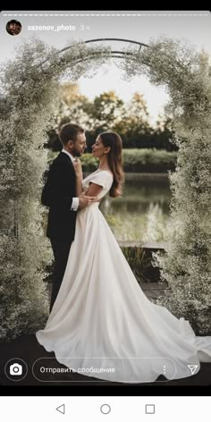 a man and woman standing next to each other in front of an arch with flowers