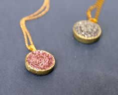 two necklaces with different colors and designs are on a blue surface, one has a gold chain