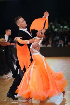 two people dressed in orange and black dancing on a dance floor with their arms around each other