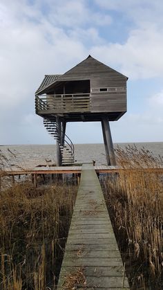 a wooden walkway leading to an observation tower on the beach with water in the background