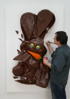 a man is painting a giant chocolate easter bunny with an orange carrot in his mouth