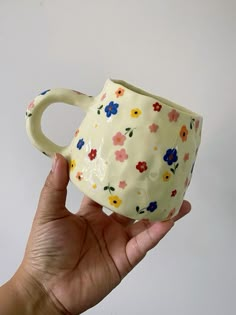 a hand holding a white coffee cup with colorful flowers on the outside and inside it