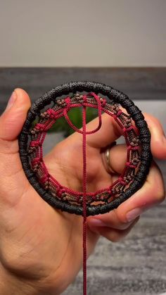 a person holding a piece of yarn with a ring on it's end, in front of a plant