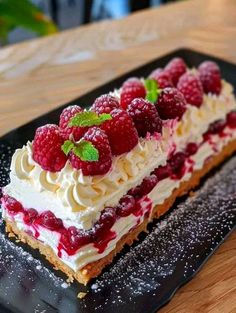 a piece of cake with raspberries and whipped cream on top sitting on a black plate