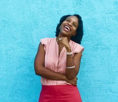 a woman standing in front of a blue wall wearing a pink shirt and red skirt