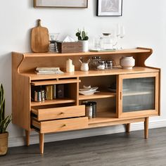 a wooden cabinet with shelves and drawers in front of a painting on the wall next to a potted plant