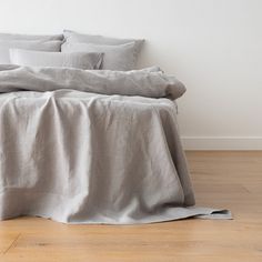 an unmade bed with grey linens and pillows