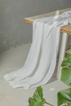 a wooden bench with a white cloth draped over it's seat and table next to it