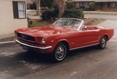 an old red mustang convertible parked in front of a house