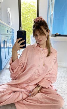 a woman sitting on the floor taking a selfie with her cell phone in a bathroom