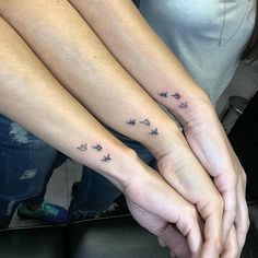 two people holding hands with small tattoos on their wrists and fingers, both showing the same direction