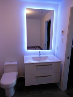 a white toilet sitting next to a sink under a bathroom mirror with blue lights on it