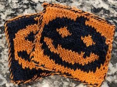 two orange and black knitted coasters sitting on top of a marble countertop