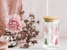 a pink flower next to a glass jar with a straw in it and a wooden lid