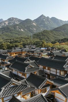 an aerial view of many buildings in front of mountains and trees with hills in the background