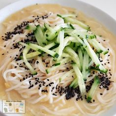 a white bowl filled with noodles and cucumber garnished in sesame seeds