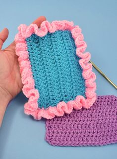 a hand is holding a crocheted piece of cloth next to a pair of knitting needles