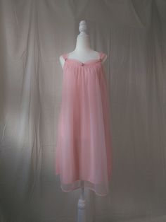 Vintage pastel pink chiffon nightgown. - Sheer overlay against nylon lining - Gorgeous gathered neckline and straps - Dainty embroidered flowers accenting the neckline - A-line silhouette - Straps are not adjustable - Era: Circa 1950s - Condition: Great; There is a slight black mark on the lining. It also seems like the hem was not finished precisely. A small part near the hem was repaired by the previous owner.  - Size: Small - Color: Pastel pink - Brand: Unknown - Measurements: 19in pit to pit, 34in length including straps - Fabric Content: 100% nylon Shown on a mannequin with a 33" bust, 26" waist, and 35" hips. Fits a size 2-4. Some garments may be clipped onto mannequin or model for display. MORE INFO: *Please, note that all items are vintage. Therefore, it is expected to find some we Disney Princess Nightgown, Regency Era Sleepwear, Sheer Coquette Bedtime Dresses, Feminine Sheer Nightgown With Spaghetti Straps, Sheer Sleeveless Coquette Nightgown, Pink Sheer Dress With Spaghetti Straps, Sheer Spaghetti Strap Bedtime Dress, Sleeveless Pink Wedding Nightgown, Pink Spaghetti Strap Dress For Wedding Night