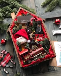 an open christmas gift box with coca cola, pine cones and other holiday decorations on a wooden table