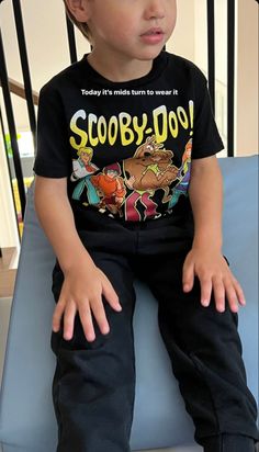 a young boy sitting on top of a blue chair wearing a black shirt with scooby doo