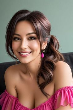 a woman with long brown hair and pink dress sitting on a couch smiling at the camera