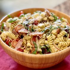 a wooden bowl filled with pasta salad on top of a red tablecloth covered table