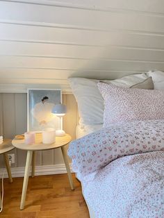 a bed with white sheets and pillows in a bedroom next to a table with two candles on it