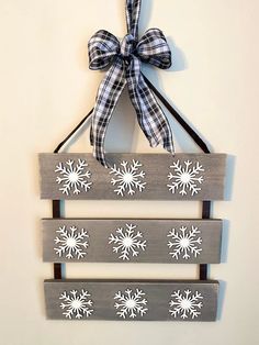 a wooden sign with snowflakes hanging from it's side and a bow on top