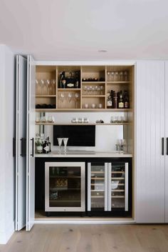 an open cabinet with wine glasses and bottles on the top shelf in front of it