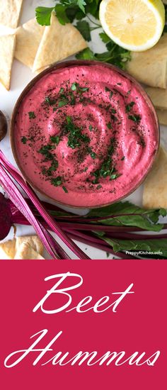 beet hummus in a bowl surrounded by crackers and lemon wedges