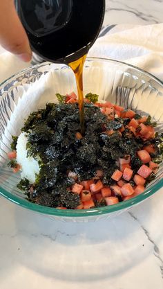 someone is pouring sauce on some food in a glass bowl with strawberries and kale