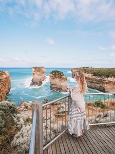 a woman standing on a balcony looking out at the ocean and rocks in the distance