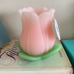 a pink glass vase sitting on top of a green plate next to a blue book