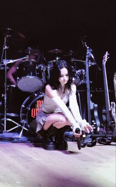 a woman kneeling on the floor next to a drum set