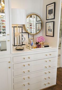 a white dresser topped with lots of drawers next to a wall filled with framed pictures