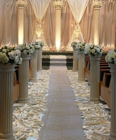 the aisle is lined with white flowers and pillars in front of an empty pew line