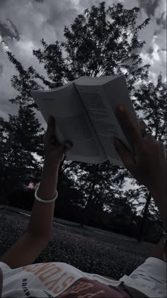 a person is reading a book in the park under a cloudy sky with trees behind them