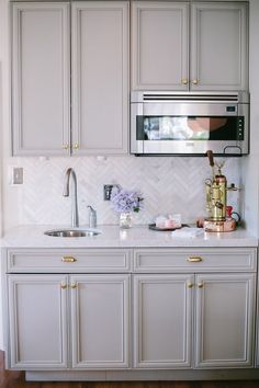 a kitchen with white cabinets and gold hardware on the countertop, along with a silver microwave oven