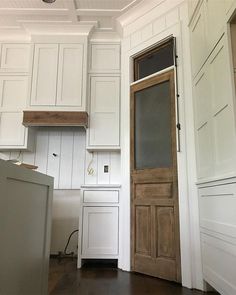 an empty kitchen with white cabinets and wood flooring on the walls, along with a wooden door