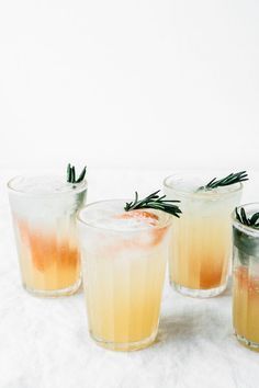 three glasses filled with drinks sitting on top of a white table covered in ice and rosemary sprigs