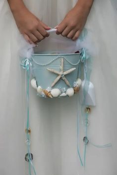 a bride holding a basket with shells and starfishs on the bottom, tied to it