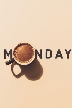 a cup of coffee sitting on top of a white table next to the word monday