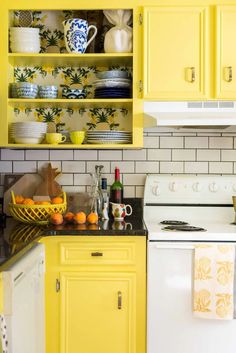 a kitchen with yellow cabinets, white appliances and dishes on the counter top in front of an oven