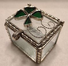 a silver box with green stained glass in the middle and an intricate design on the lid