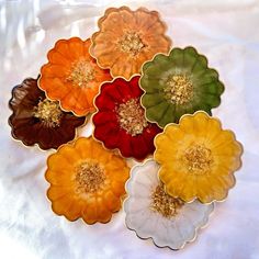 four different colored flower shaped plates on a white tablecloth with gold trimmings