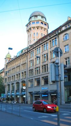 a red car is driving down the street in front of an old building with a dome on top