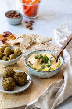 a table topped with bowls filled with dip and olives next to pita bread